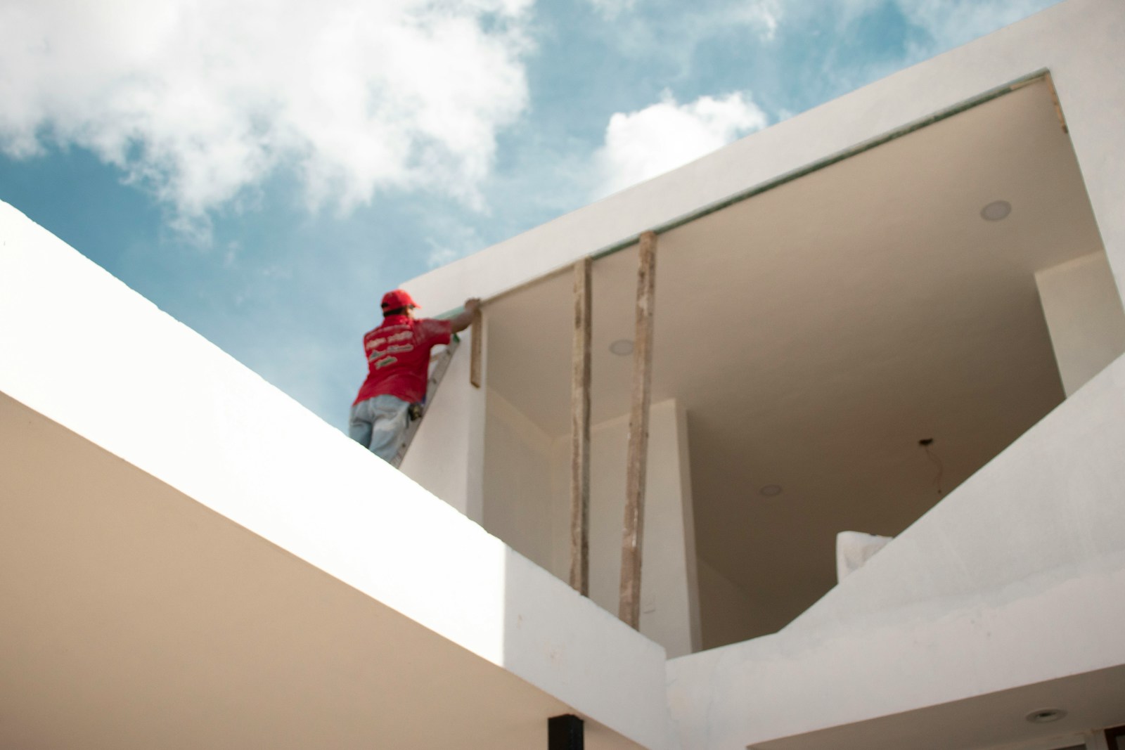 Multigest Alicante man in red jacket standing on white concrete building under blue and white cloudy sky during